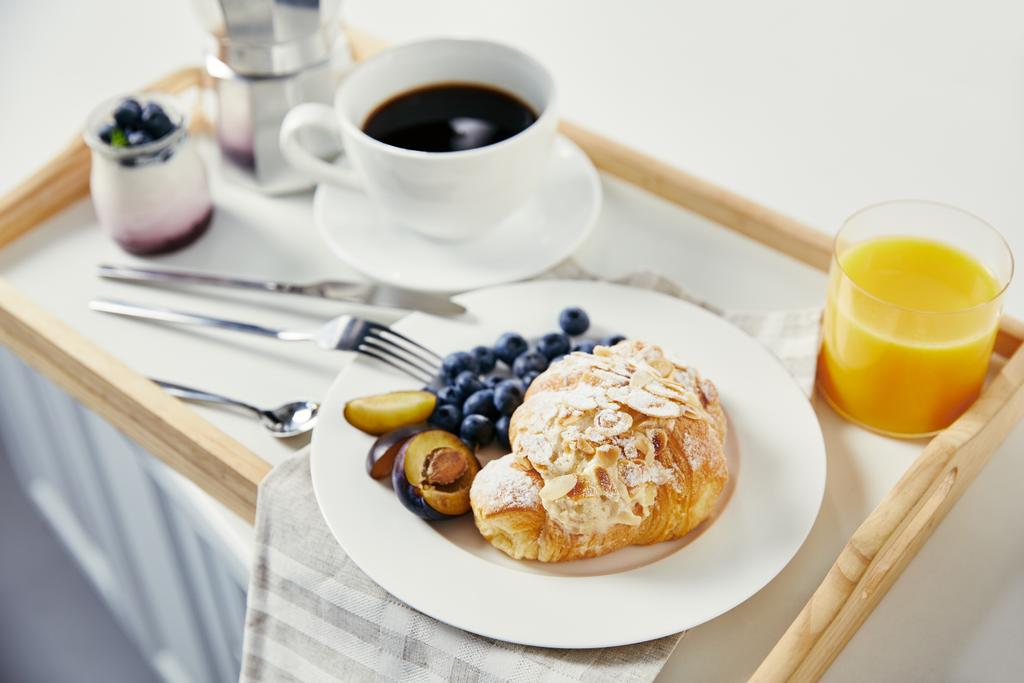 zbliżenie rogalik z świeże jagody i kawałki śliwka, szklanka soku, kawy i jogurtu na śniadanie na drewniana Taca na białym stole - Zdjęcie, obraz