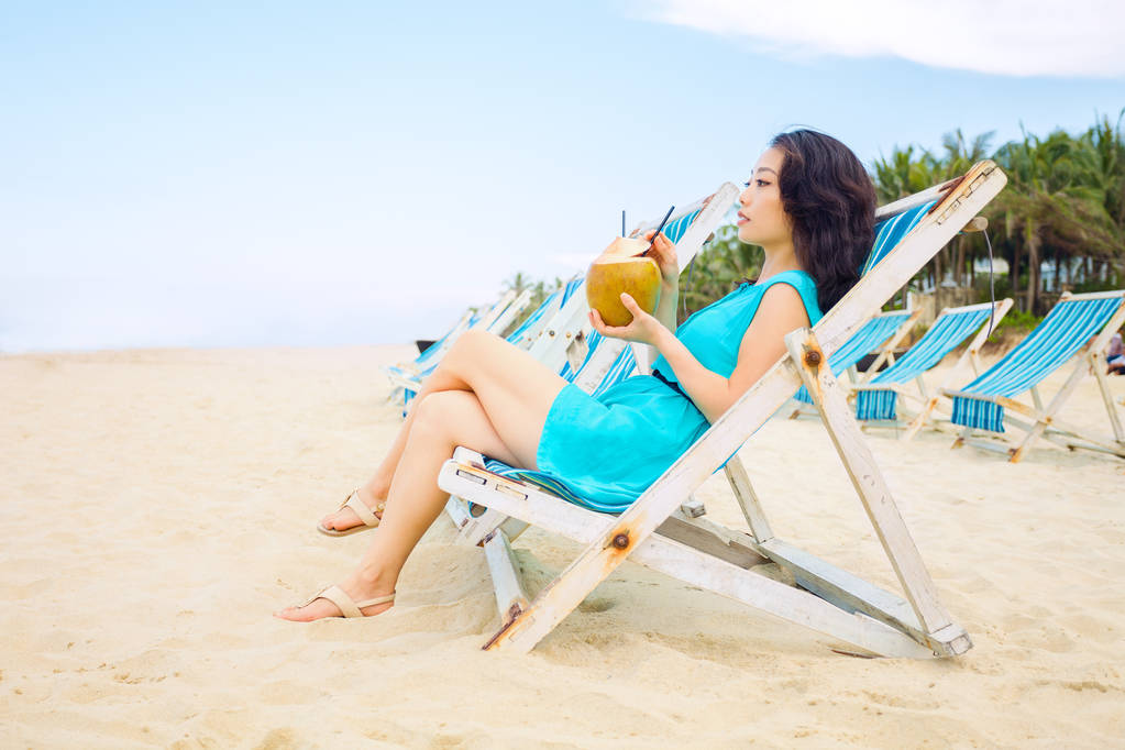 junge schöne asiatische Frau trinkt Kokossaft am Strand des tropischen Meeres - Foto, Bild