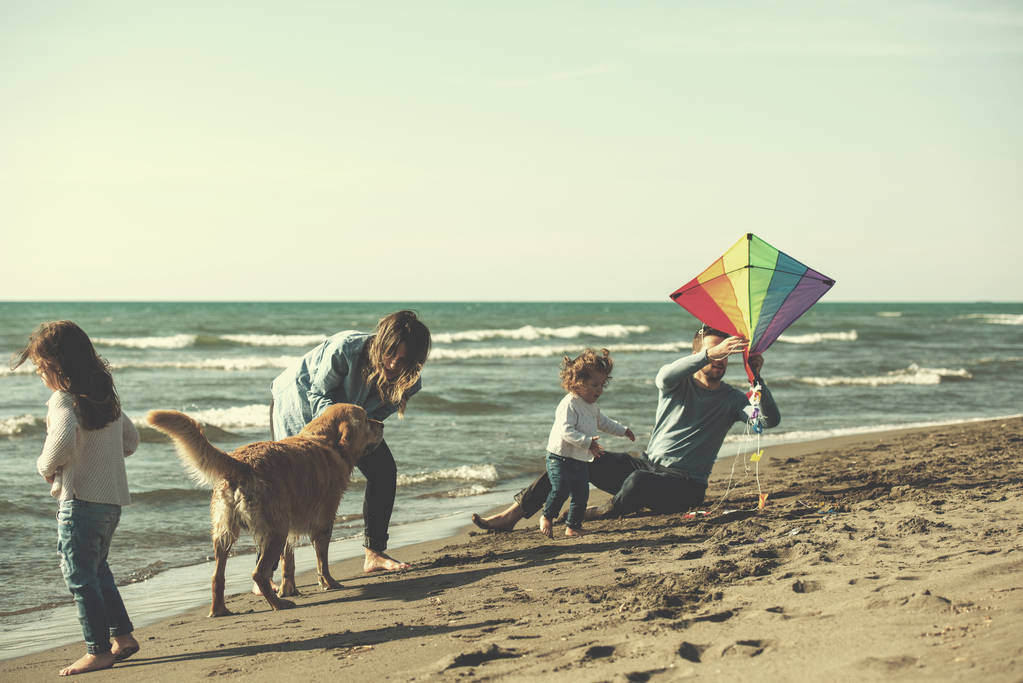 szczęśliwa młoda rodzina z dziećmi bawiąc się z psem i latawcem na plaży podczas filtra jesiennego dnia - Zdjęcie, obraz