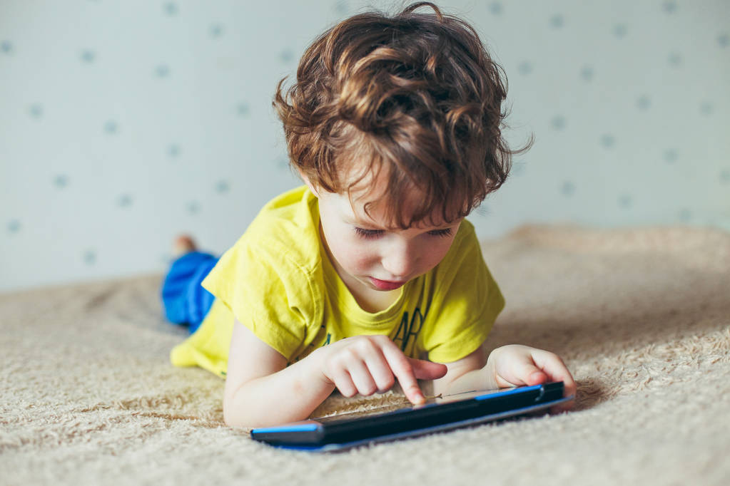 Petit garçon mignon dans un T-shirt vert jouer à des jeux sur une tablette et regarder des dessins animés
 - Photo, image