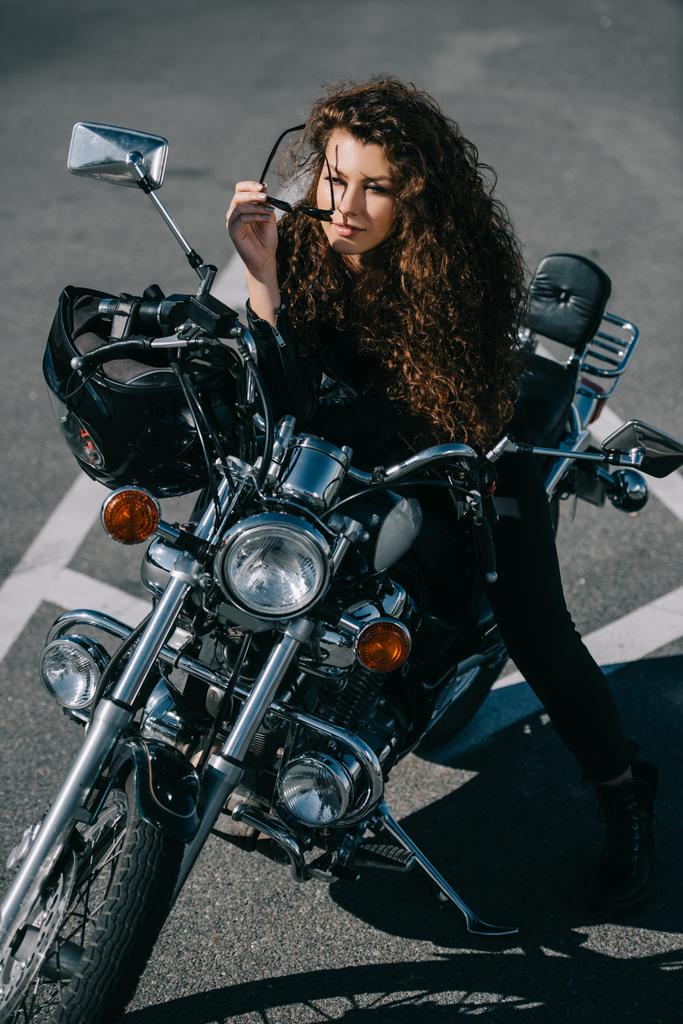 curly woman sitting on chopper motorbike with helmet on urban parking - Photo, Image