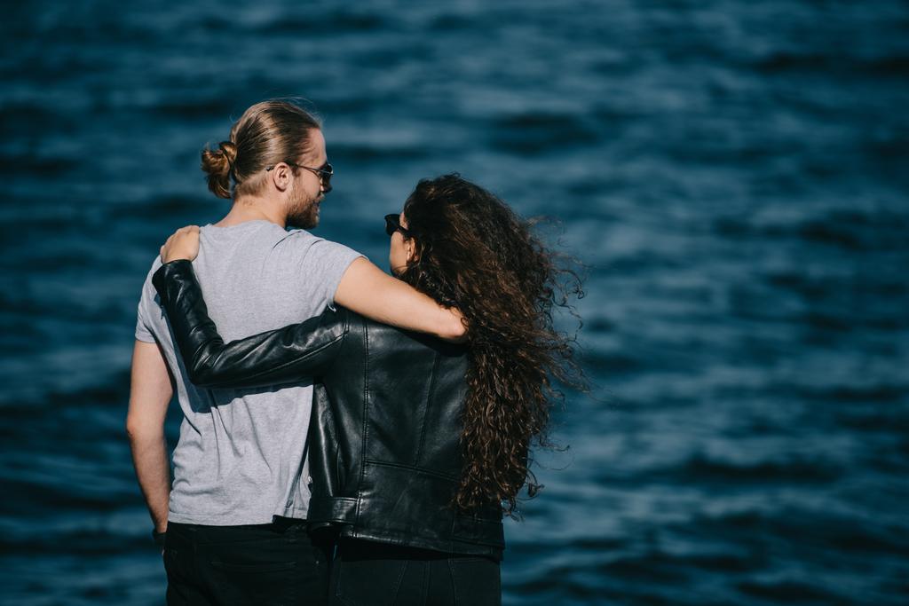vista trasera de pareja joven abrazándose cerca del mar
 - Foto, Imagen