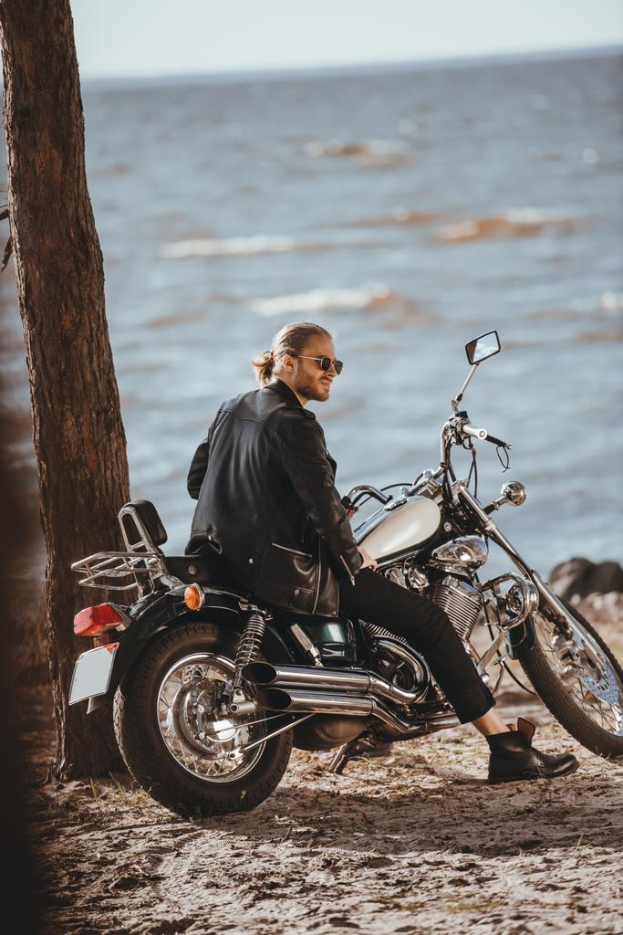 海のそばの古典的なチョッパー バイクの上に座って黒い革のジャケットのバイク - 写真・画像