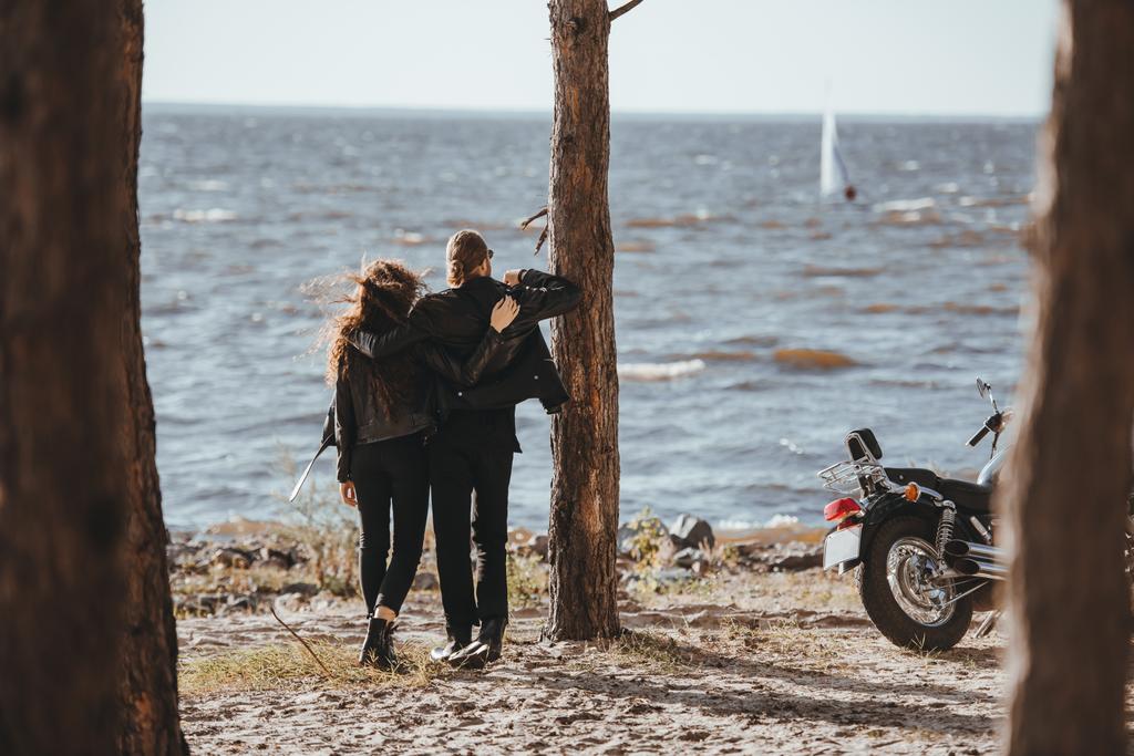 vista posteriore di coppia di motociclisti che abbracciano e guardano il mare, moto in piedi vicino
 - Foto, immagini