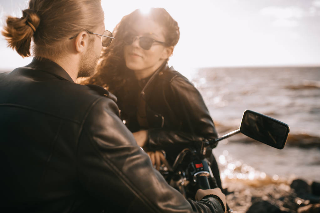 Mädchen flirtet mit Biker, während er auf Motorrad in der Nähe des Meeres mit Rücklicht sitzt - Foto, Bild