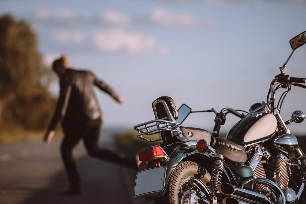 Zerbrochenes klassisches Motorrad auf der Straße mit wütendem Biker im Hintergrund, selektiver Fokus - Foto, Bild