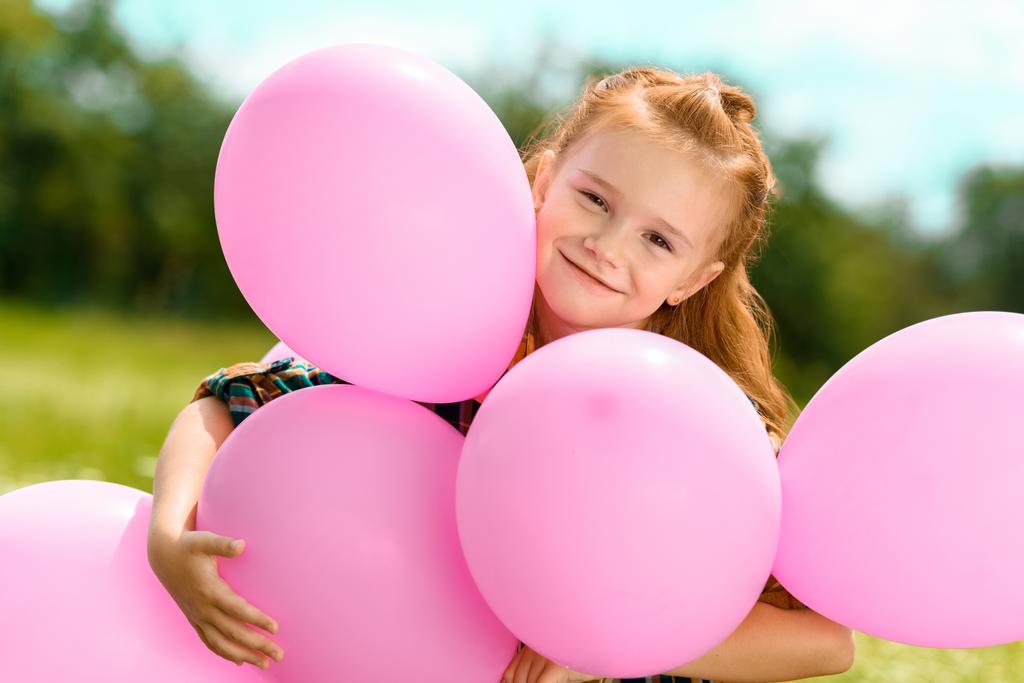 πορτρέτο του χαμογελώντας χαριτωμένο παιδί αγκάλιασμα ροζ μπαλόνια στο πεδίο του καλοκαιριού - Φωτογραφία, εικόνα