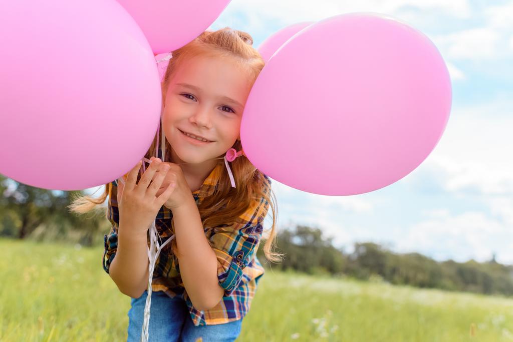 portrait of cute child with pink balloons looking at camera in summer field - Photo, Image
