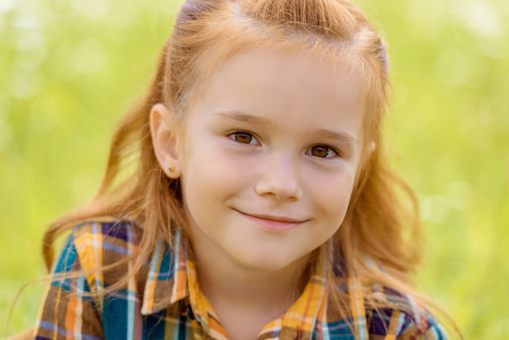 Porträt eines entzückenden Kindes, das in die Kamera blickt, mit verschwommenem grünen Gras auf dem Hintergrund - Foto, Bild