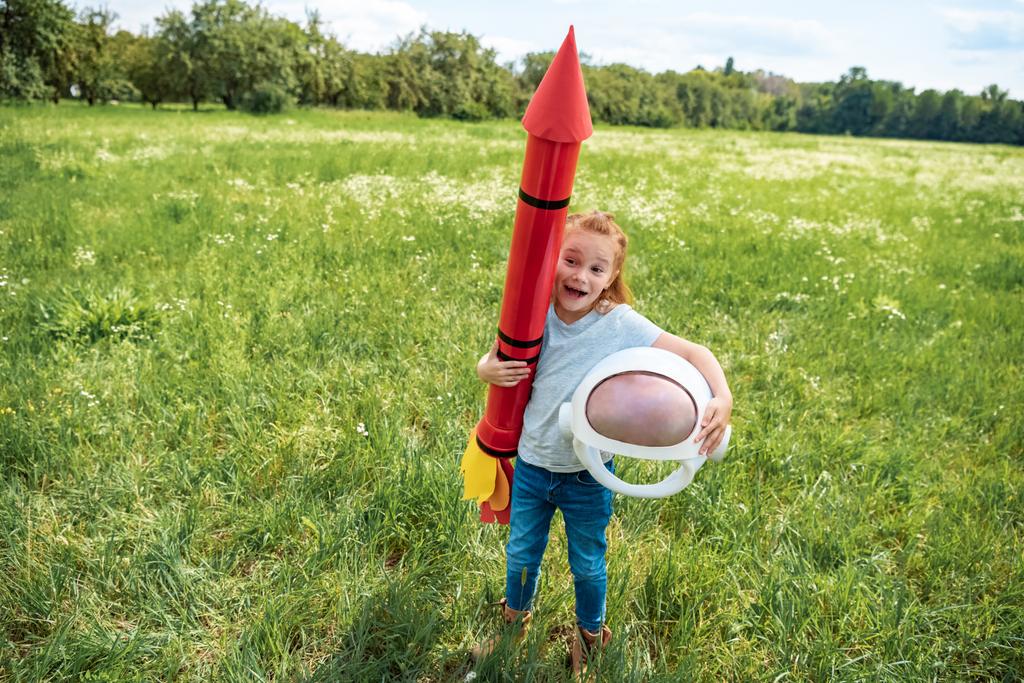 cabellera roja excitada con cohete y casco astronauta de pie en el campo de verano
 - Foto, imagen
