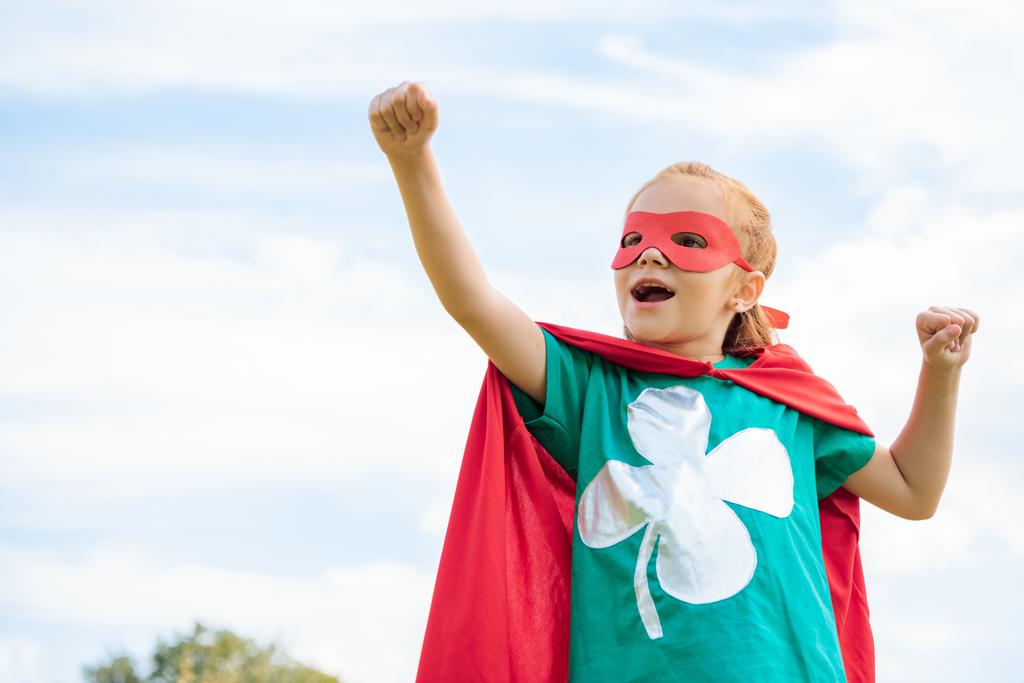 adorable enfant en costume de super-héros avec bras étendu et ciel nuageux bleu sur fond
 - Photo, image