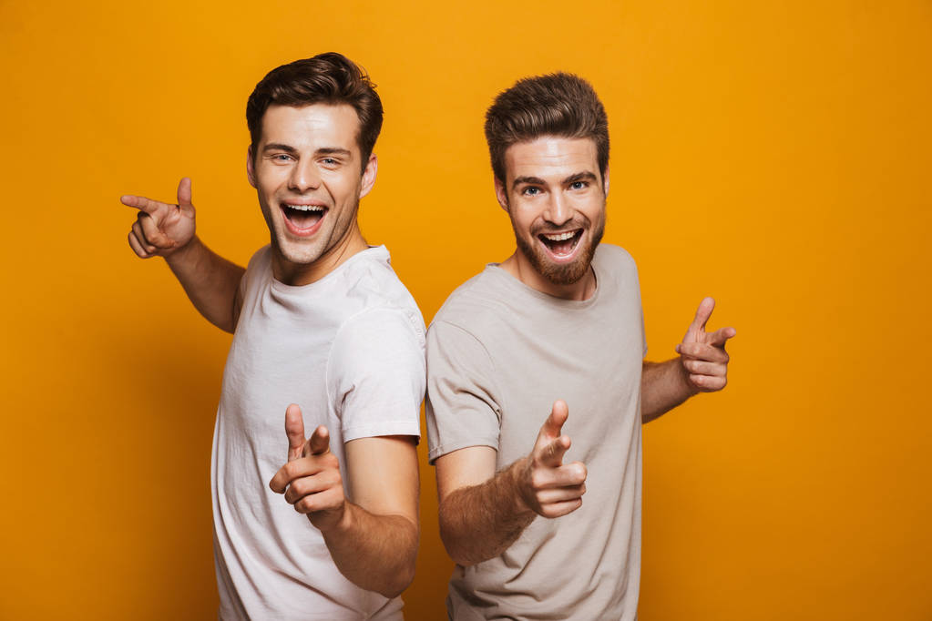 Πορτρέτο του σε δύο νεαρούς άνδρες ευτυχισμένη καλύτεροι φίλοι επισημαίνοντας δάχτυλα στο φωτογραφική μηχανή που απομονώνονται σε κίτρινο φόντο - Φωτογραφία, εικόνα