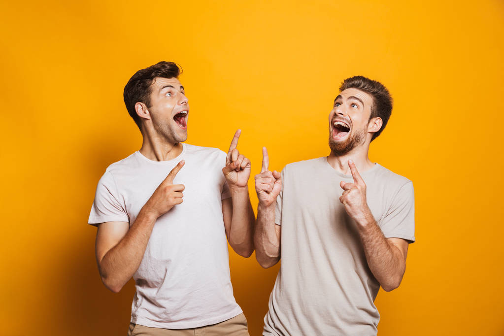 Porträt zweier aufgeregter junger Männer beste Freunde, die mit dem Finger auf Kopierraum zeigen, isoliert über gelbem Hintergrund - Foto, Bild