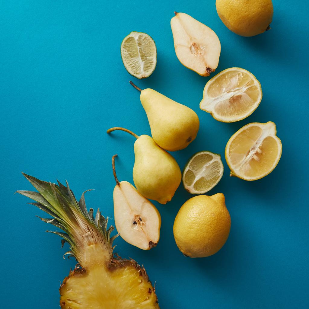 Draufsicht auf reife Ananas, Birnen und Zitronen auf blauer Oberfläche  - Foto, Bild