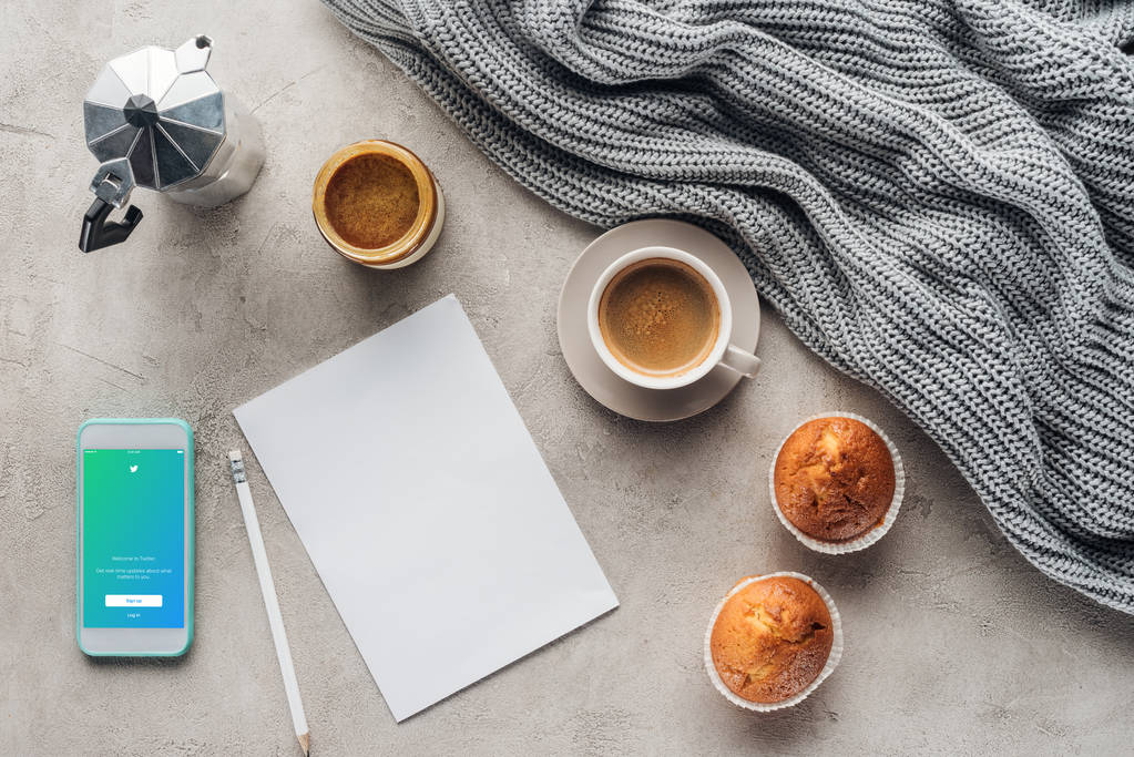 felülnézet csésze kávé muffin, üres papír és smartphone-val twitter app képernyőjén a betonfelület a drapéria kötött gyapjú - Fotó, kép