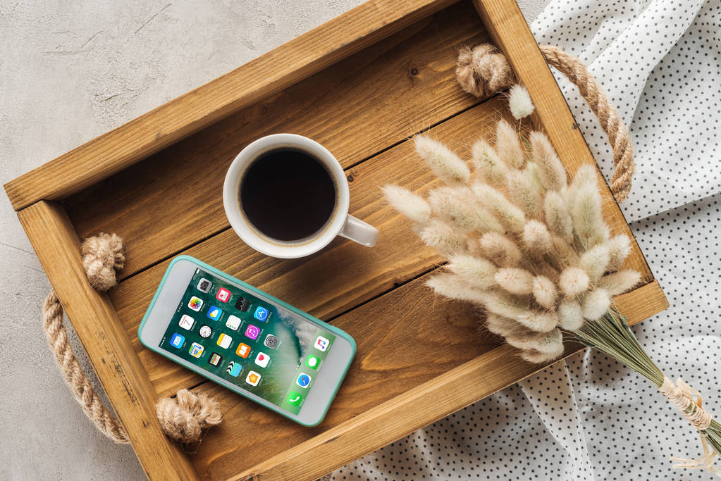 vista superior da xícara de café e smartphone com iOS homescreen site na tela na bandeja com buquê de lagurus ovatus na superfície de concreto
 - Foto, Imagem
