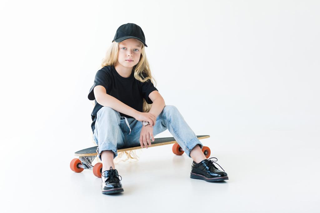 full length view of child with long curly hair sitting on longboard and looking at camera isolated on white  - Photo, Image