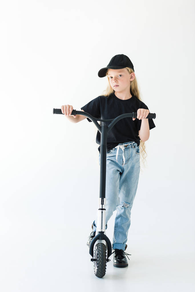 mooie jongen in zwart t-shirt en cap scooter rijden en kijken naar camera geïsoleerd op wit   - Foto, afbeelding