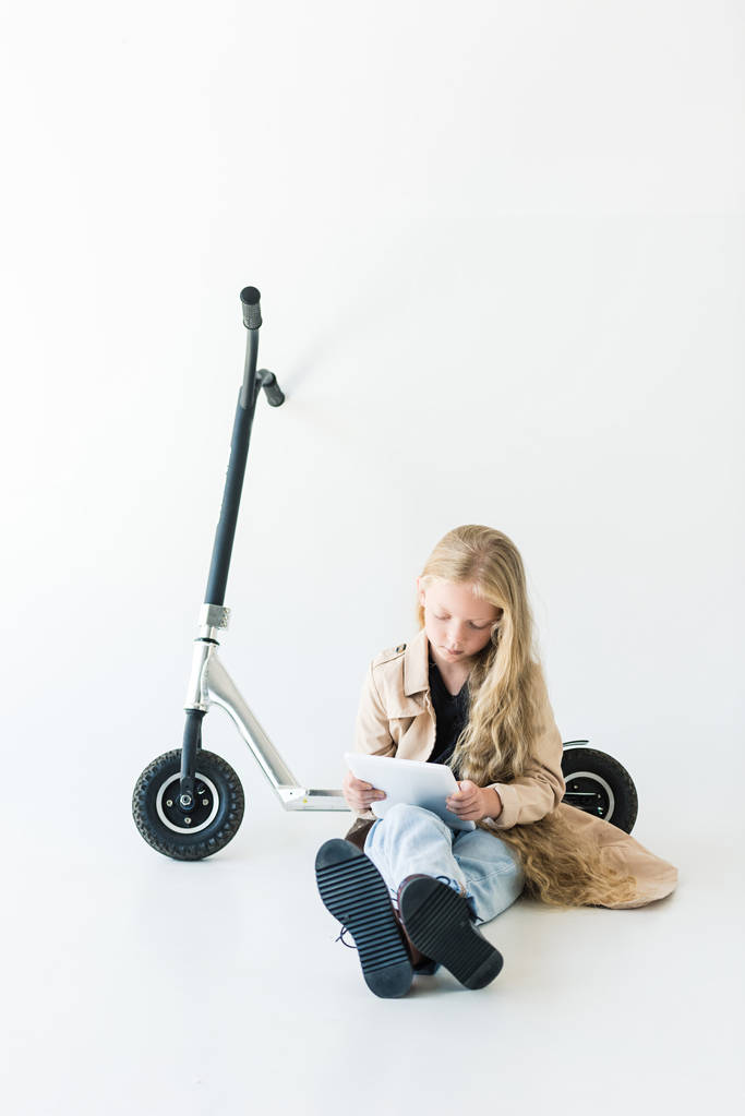 adorable enfant avec de longs cheveux bouclés en utilisant une tablette numérique tout en étant assis près de scooter isolé sur blanc
  - Photo, image