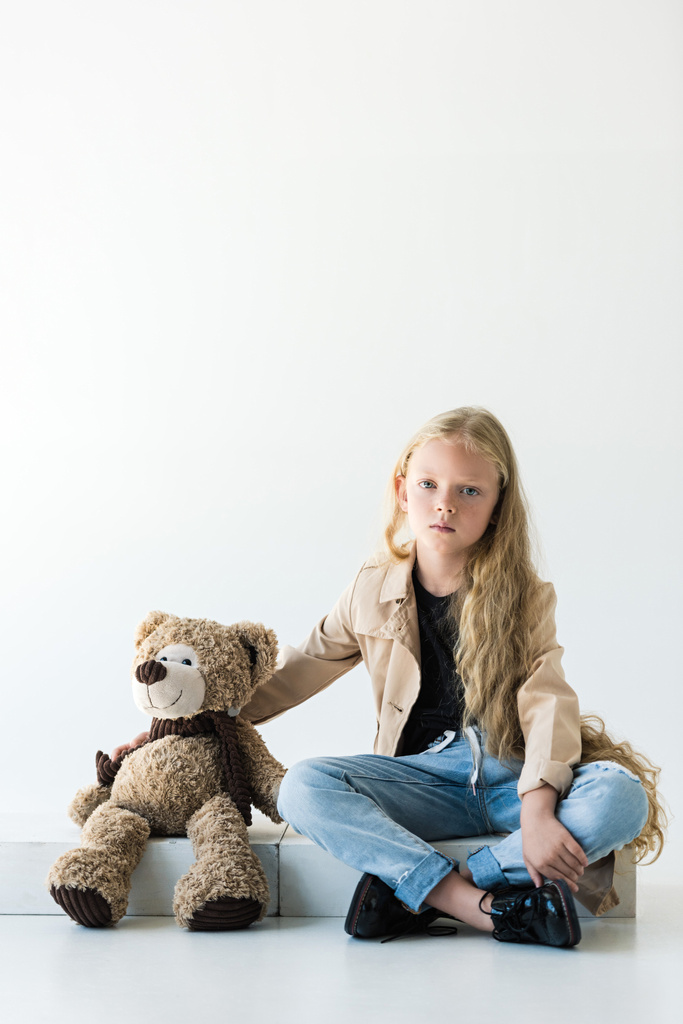 linda criança olhando para a câmera enquanto sentado com ursinho de pelúcia no branco
 - Foto, Imagem