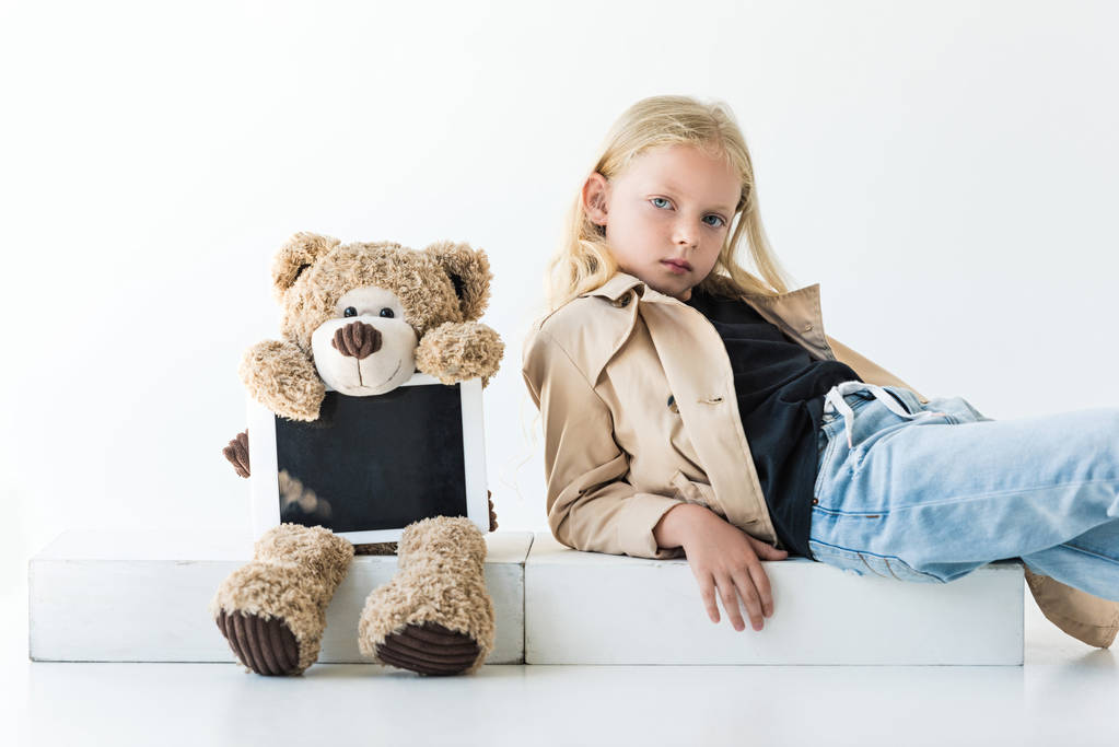 Teddybär mit digitalem Tablet und entzückendem stilvollem Kind, das in die Kamera auf weiß schaut - Foto, Bild