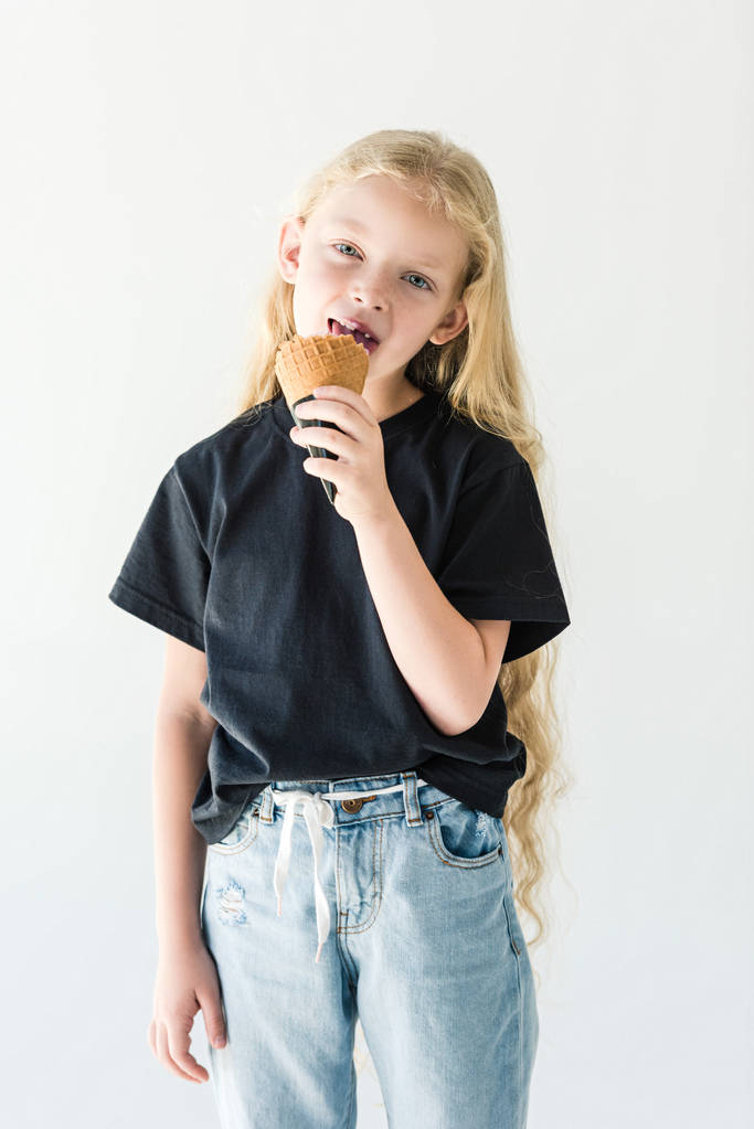 krásné dítě s dlouhými kudrnatými vlasy, jíst zmrzlinu a při pohledu na fotoaparát izolované na bílém - Fotografie, Obrázek