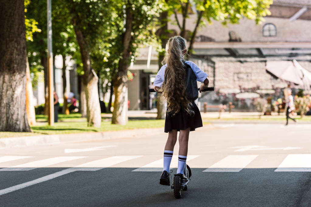 aranyos kis gyerek, a lovaglás scooter street hátizsák hátsó nézet  - Fotó, kép