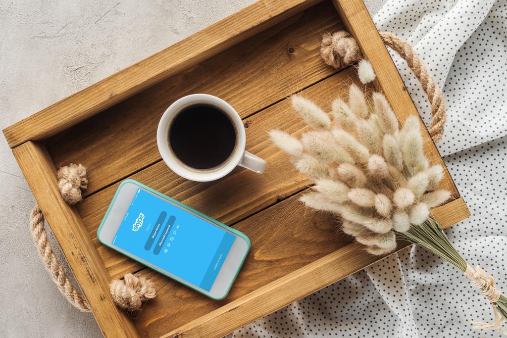 pohled shora na šálek kávy a smartphone s aplikaci skype na obrazovce na zásobník s lagurus ovatus kytice na betonový podklad - Fotografie, Obrázek