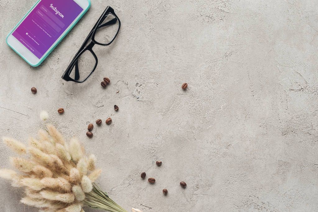 κάτοψη του smartphone με την εφαρμογή instagram στην οθόνη με γυαλιά, έχουν χυθεί καφές και lagurus ovatus μπουκέτο στην επιφάνεια του σκυροδέματος - Φωτογραφία, εικόνα