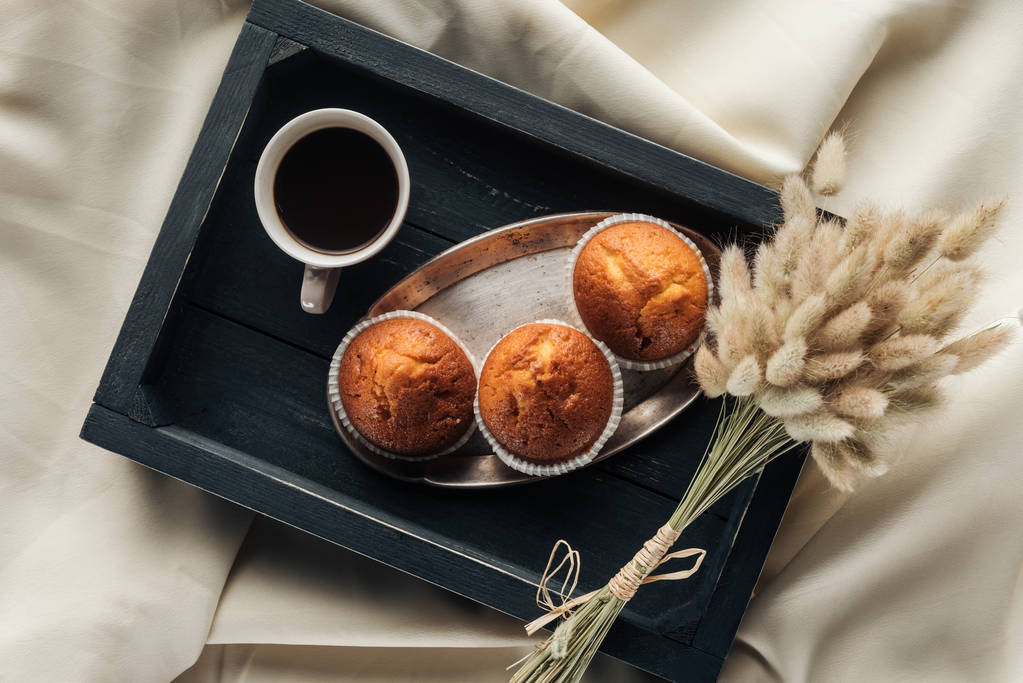 vista superior de café e muffins na bandeja com buquê de lagurus ovatus em pano bege, café da manhã no conceito de cama
 - Foto, Imagem