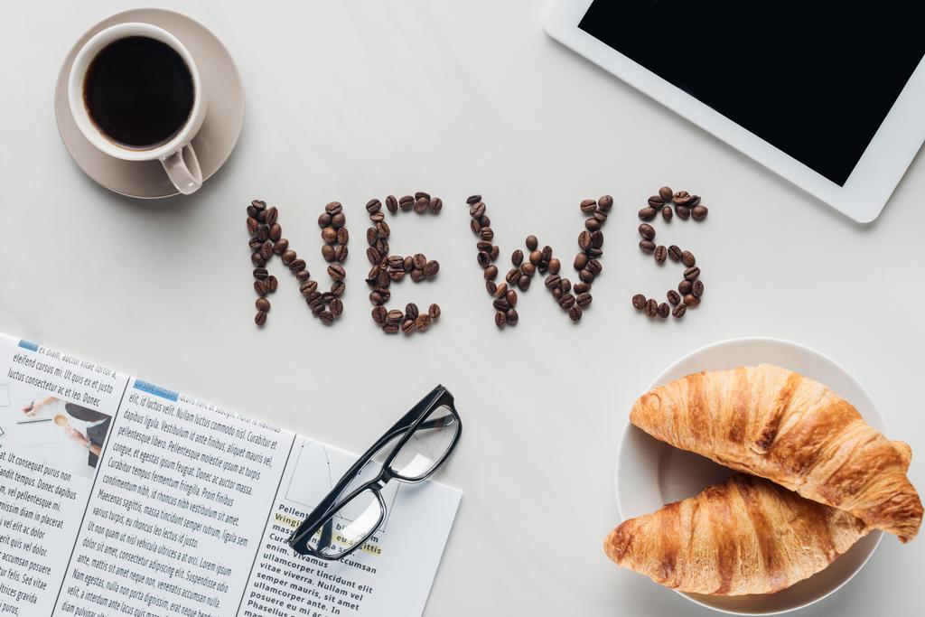 vista superior del café con letras de noticias hechas de granos de café, croissants y periódico con la tableta en mármol blanco
 - Foto, imagen