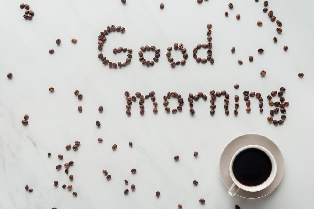 vista superior de la taza de delicioso café y letras de buenos días hechas de granos de café en mármol blanco
 - Foto, Imagen