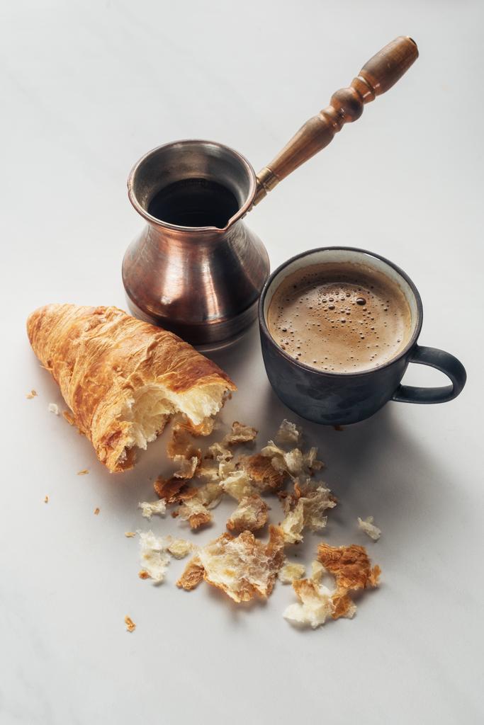 Close-up shot šálek kávy s cezve a pokousal croissant na bílém mramoru - Fotografie, Obrázek