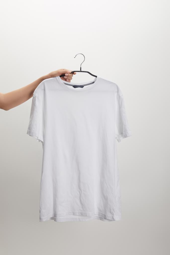 abgeschnittenes Bild einer Frau mit Kleiderbügel und weißem Hemd auf weißem Hintergrund - Foto, Bild