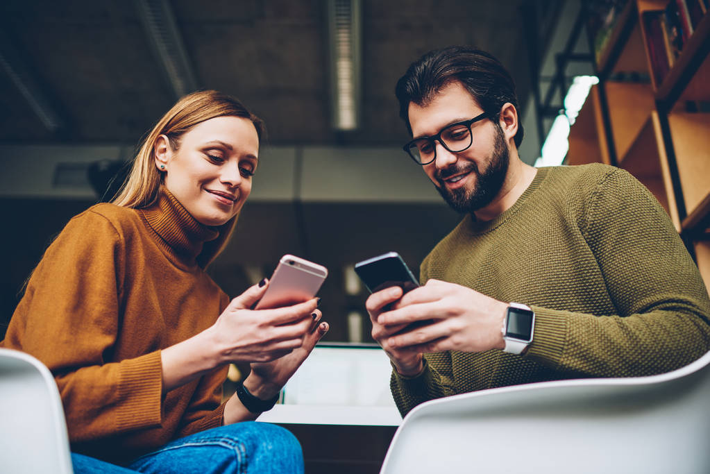 Δύο νέοι χρήστες ξέγνοιαστες κουβεντιάζοντας με follovers στο κοινωνικό δίκτυο μέσω τηλέφωνα, των Χίπστερς μαθητών δημιουργώντας δημοσίευση και αναζήτηση πληροφοριών μέσω κινητών τηλεφώνων, ενώ κάθεται στην τάξη - Φωτογραφία, εικόνα