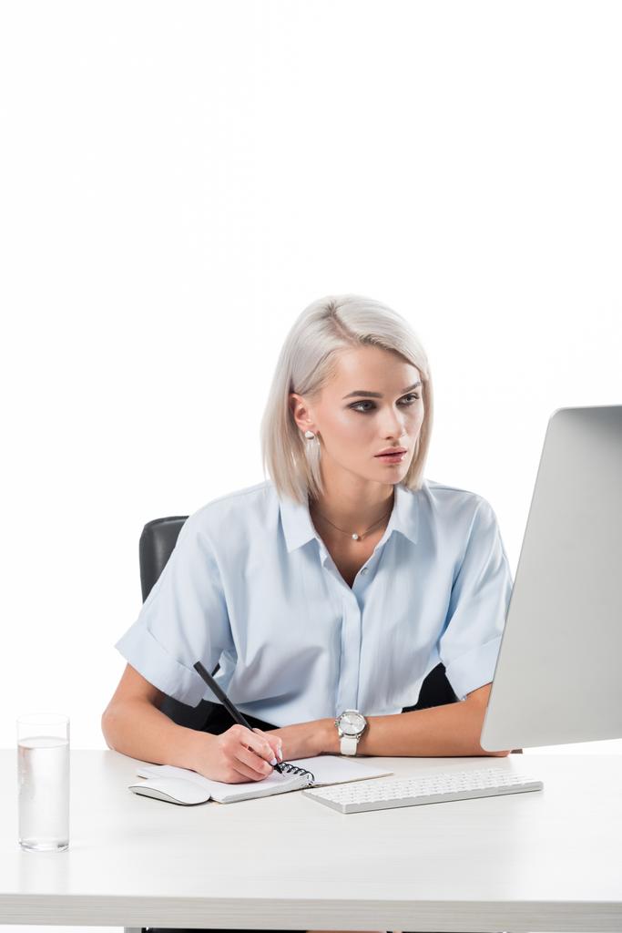 портрет фокусованої бізнес-леді, що працює на робочому місці зі склянкою води, ноутбука та екрану комп'ютера ізольовані на білому
 - Фото, зображення