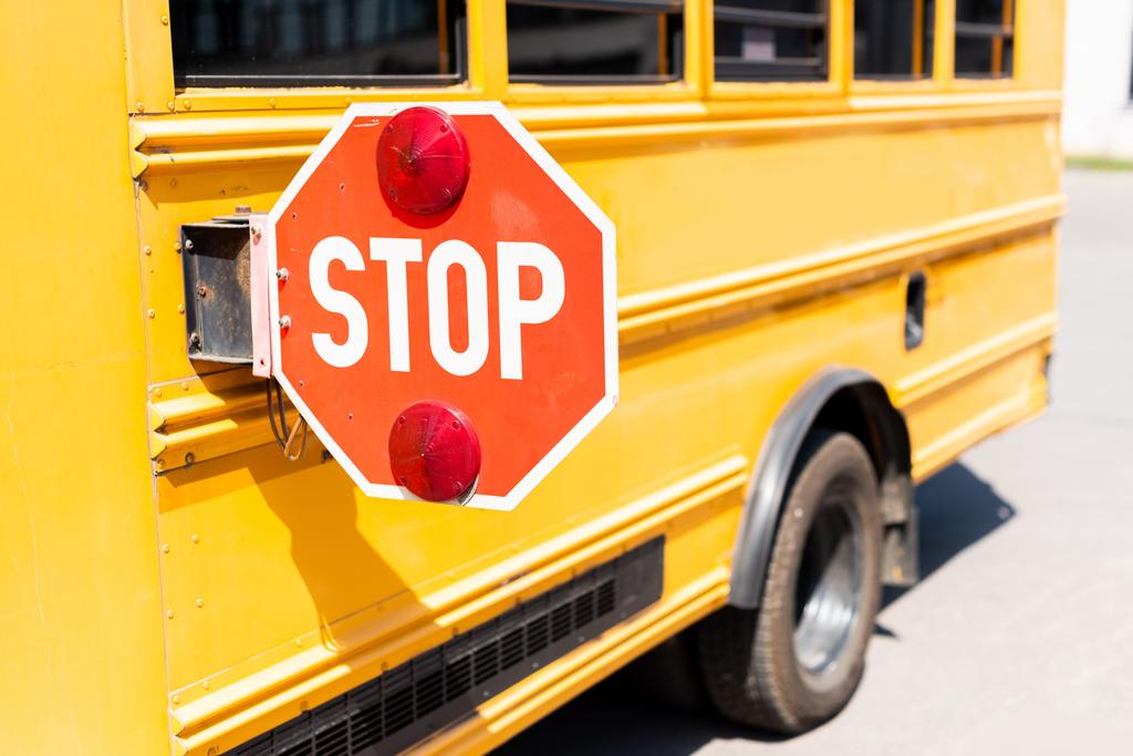 bijgesneden schot van traditionele schoolbus met stop verkeersbord - Foto, afbeelding