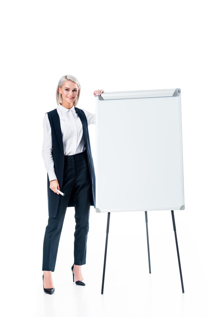 usměvavá podnikatelka v formální oblečení, stojící poblíž prázdné tabule izolované na bílém - Fotografie, Obrázek