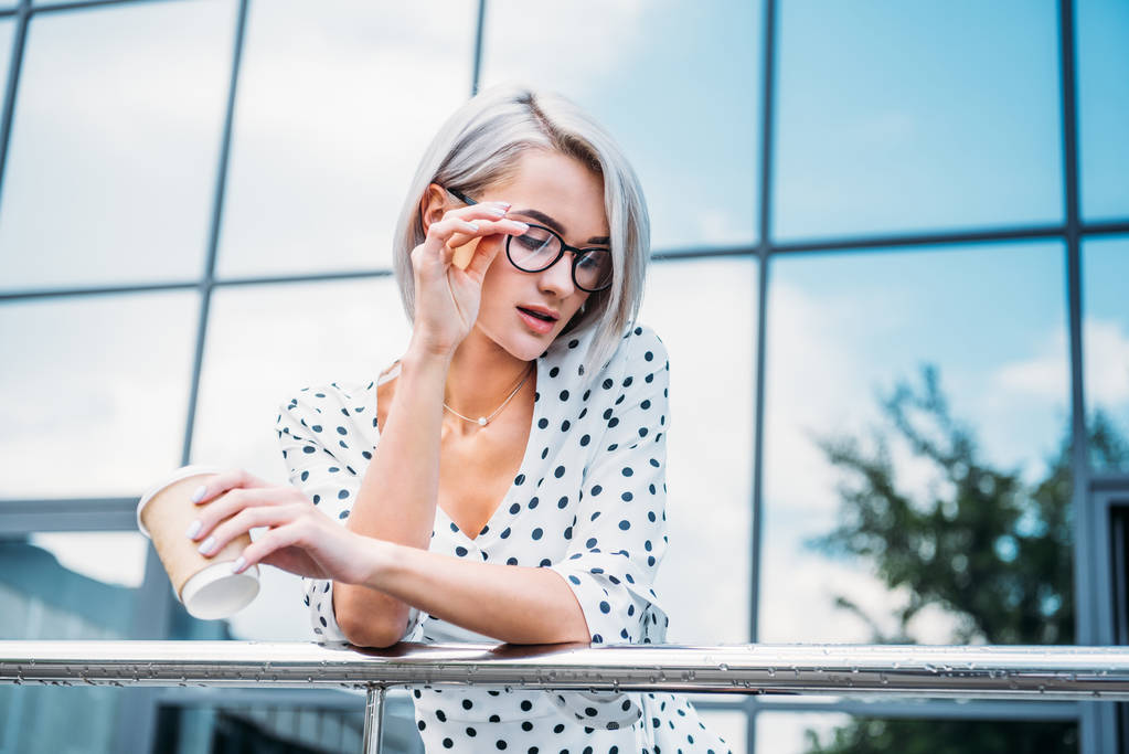 Portret van stijlvolle zakenvrouw in brillen met koffie te gaan in de hand op straat - Foto, afbeelding