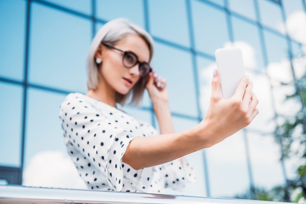 selective focus of businesswoman in eyeglasses taking selfie on smartphone in hand on street - Photo, Image