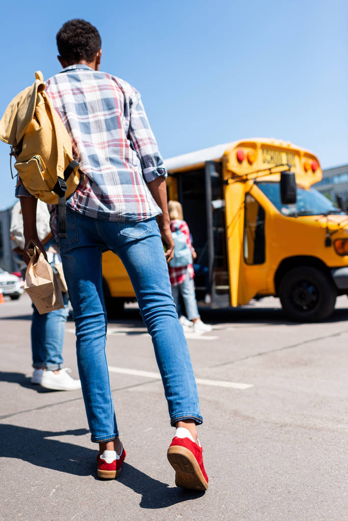 Rückansicht eines Teenagers, der an einem Schulbus läuft - Foto, Bild