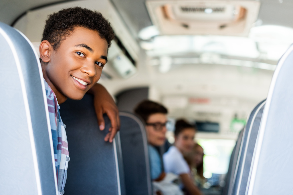 teini-ikäiset oppilaat istuvat koulubussissa ja katsovat taaksepäin kameraan
 - Valokuva, kuva