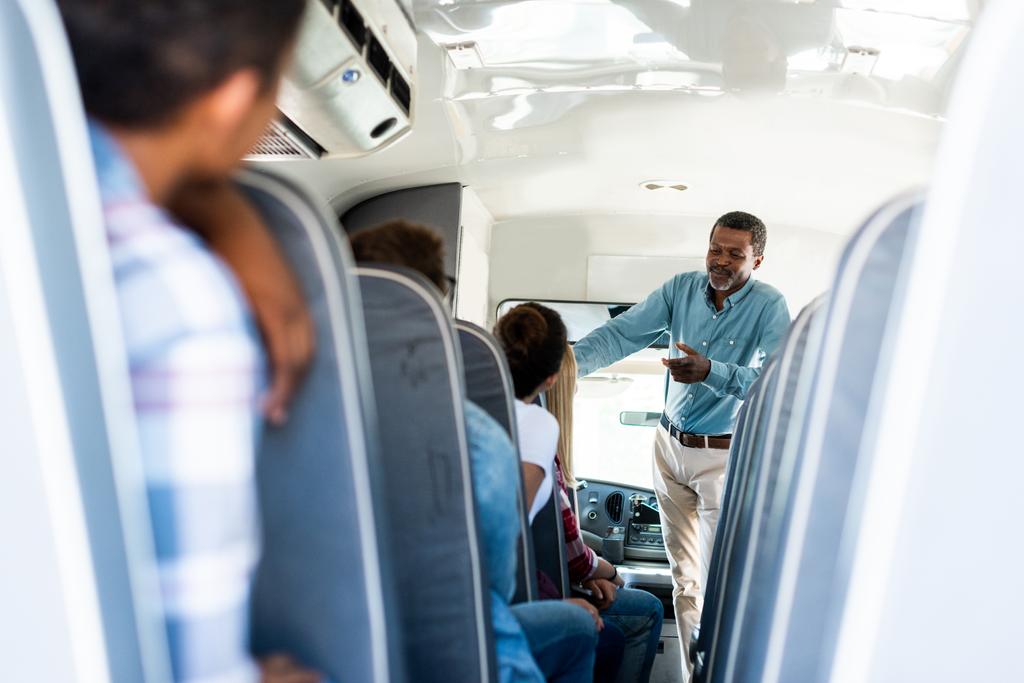 vista trasera de estudiantes adolescentes sentados en el autobús escolar y escuchando a un profesor afroamericano maduro
 - Foto, imagen