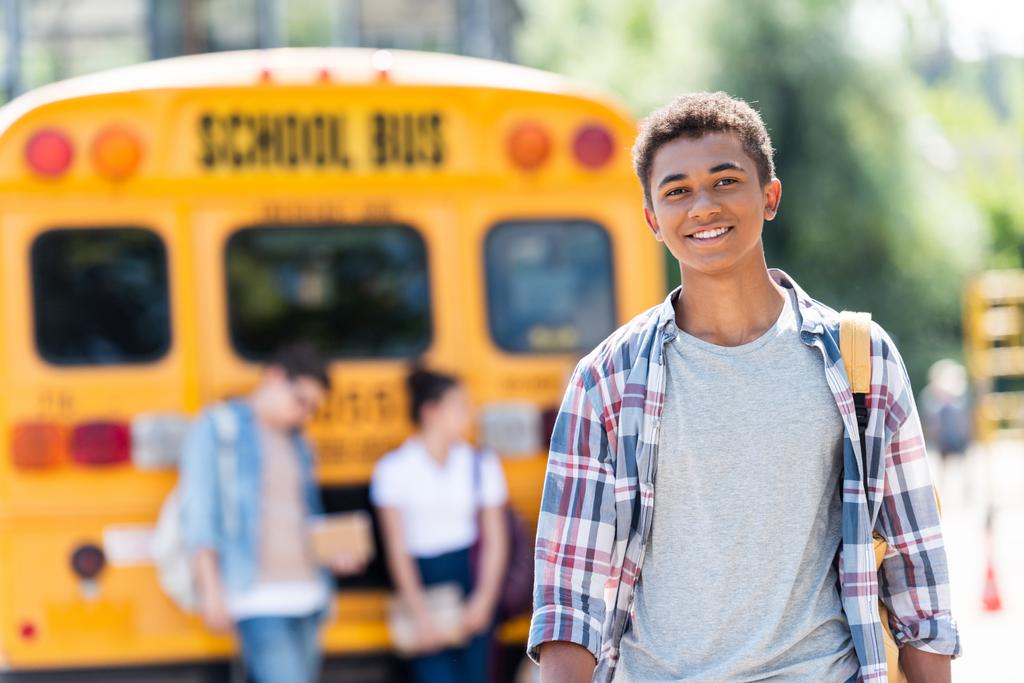heureux adolescent afro-américain écolier regardant caméra en face de bus scolaire
 - Photo, image