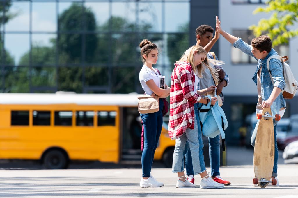 grupo de estudiantes adolescentes que dan cinco en el estacionamiento frente al autobús escolar
 - Foto, Imagen