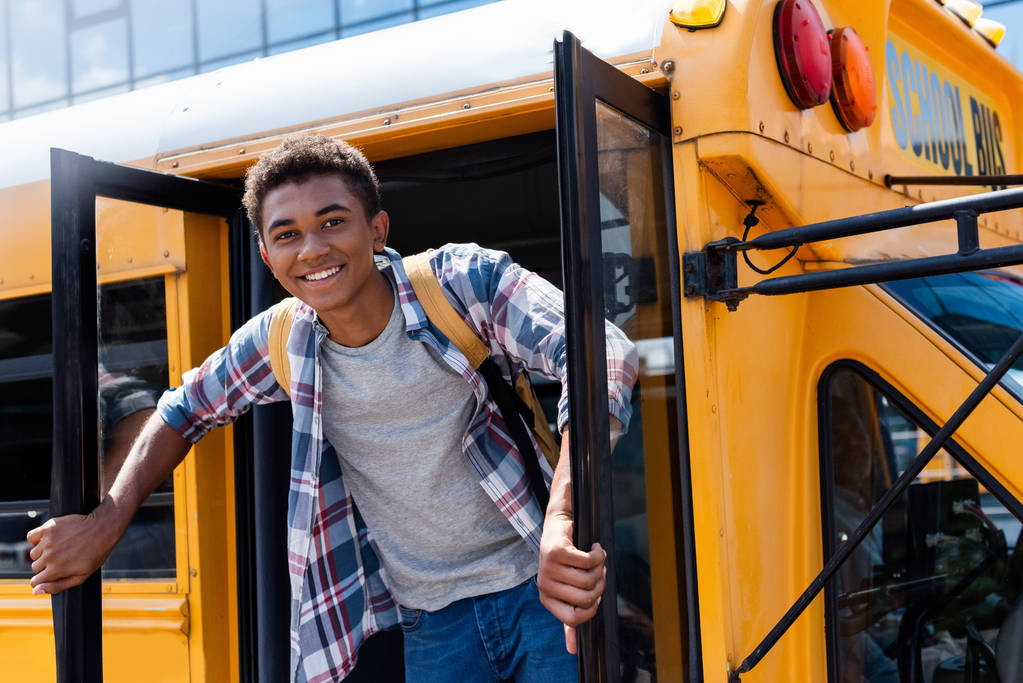 šťastné teen africké americké školák stojící ve dveřích školního autobusu a při pohledu na fotoaparát - Fotografie, Obrázek