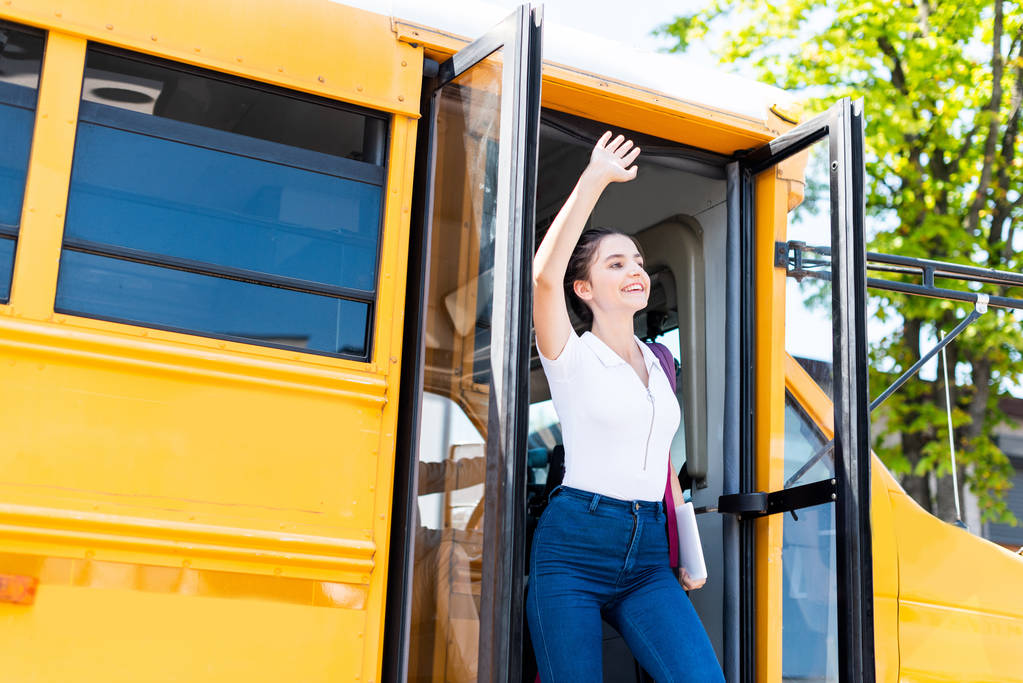 Gelukkig tiener schoolmeisje lopen uit schoolbus en zwaaien - Foto, afbeelding