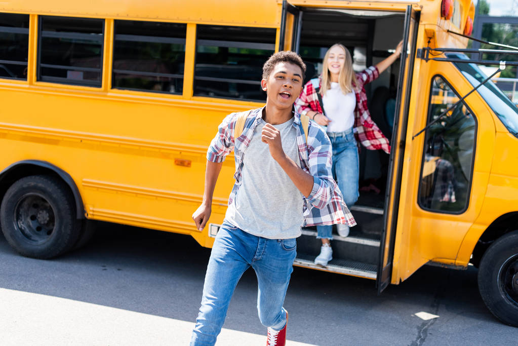 multiétnicos adolescentes estudiantes pareja corriendo fuera de autobús escolar
 - Foto, imagen