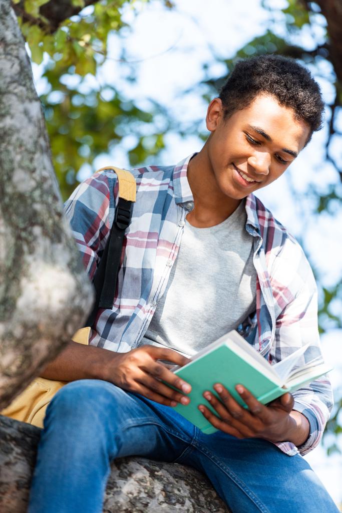 κάτω όψη της ευτυχής έφηβος μαθητής Αλφαβητάριον κάτω από δέντρο - Φωτογραφία, εικόνα