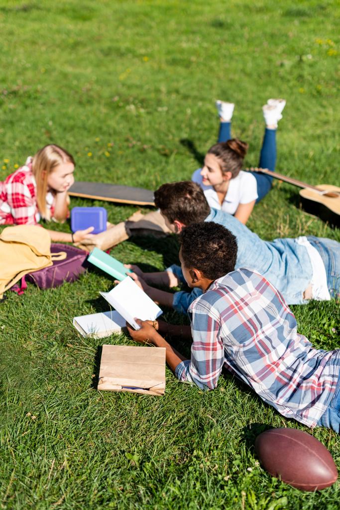 grupo de adolescentes eruditos acostados en la hierba y estudiando juntos
 - Foto, Imagen
